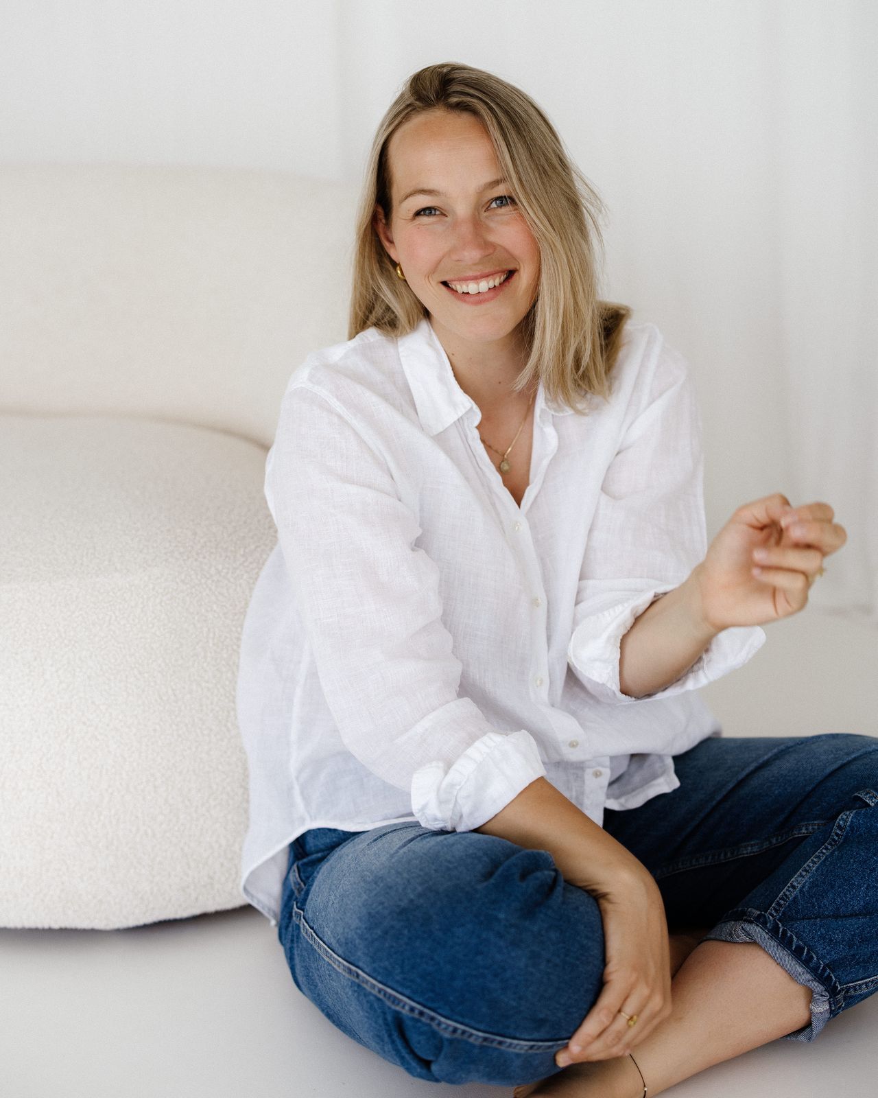 Elena Stark sitzt entspannt und lachend im Schneidersitz auf dem Boden vor einem hellen Sofa