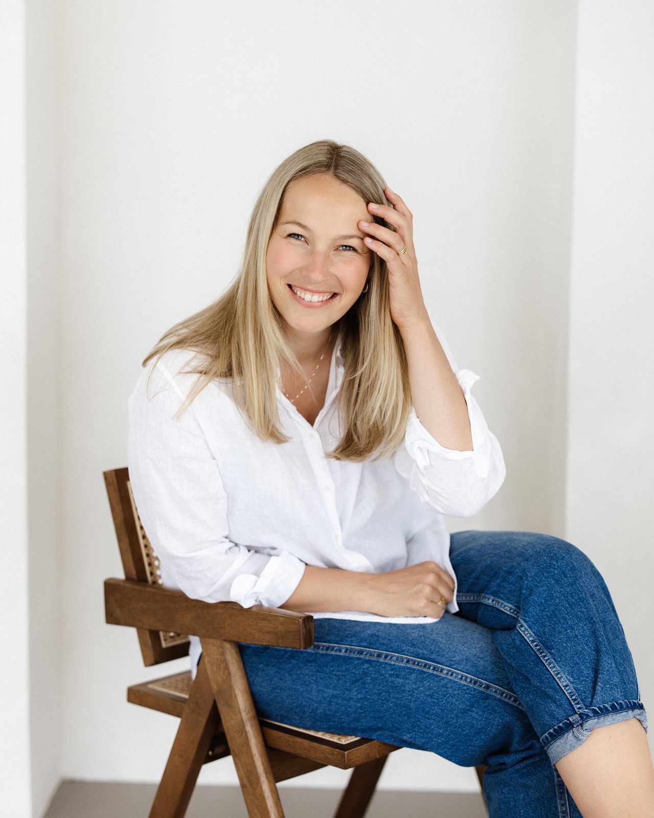 Elena Stark – Coaching bei Reutlingen: Elena sitzt lächelnd auf einem Holzstuhl mit Wiener Geflecht, eine Hand im Haar